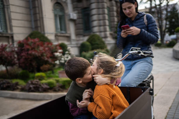 Kids playing in cargo bike Little brother and sister having fun in cargo bicycle on the street city, their mother is sitting on a bicycle. three way kiss stock pictures, royalty-free photos & images
