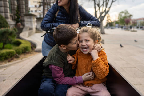 Kids playing in cargo bike Little brother and sister having fun in cargo bicycle on the street city, their mother is sitting on a bicycle. three way kiss stock pictures, royalty-free photos & images
