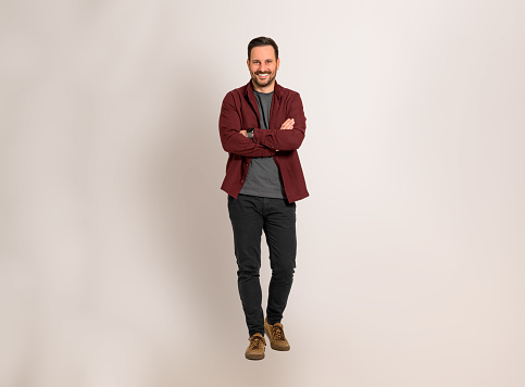 Portrait of happy young businessman with arms crossed posing confidently against isolated background. Handsome male entrepreneur dressed in maroon shirt smiling and looking at camera