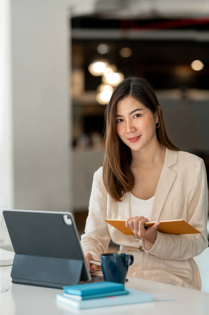 istock Businesswoman using a laptop, smiling and looking at the camera while sitting at an office desk in a modern office. 1489768097