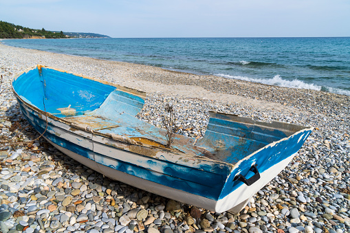 An abandoned broken boat full of holes lying on the seashore in the off season