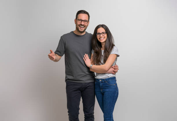 retrato de una alegre pareja romántica de jóvenes tomados de la mano y mirando a la cámara. novio y novia alegres con anteojos y casuales sonriendo y posando contra el fondo - heterosexual couple fotografías e imágenes de stock