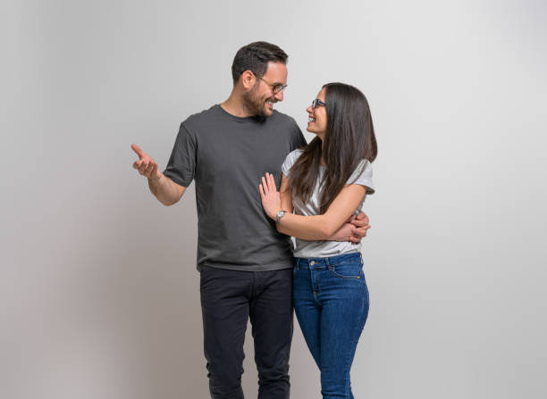 istock Joyful loving young man embracing girlfriend while standing against isolated background. Romantic couple wearing eyeglasses and casuals looking at each other affectionately 1489769461