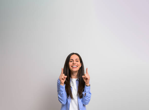 Portrait of happy female manager pointing fingers upwards at copy space for marketing on background. Young woman smiling and showing empty space for advertising Portrait of happy female manager pointing fingers upwards at copy space for marketing on background. Young woman smiling and showing empty space for advertising spokesmodel stock pictures, royalty-free photos & images