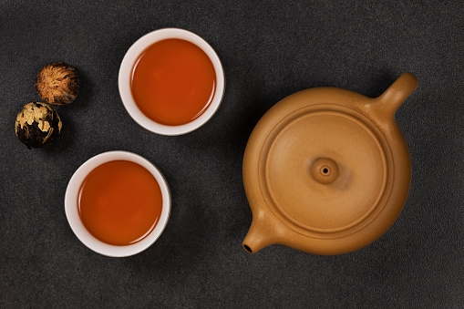 Yellow-orange tea in clay cups against the background of a ceramic teapot and Chinese tea balls. View from above.