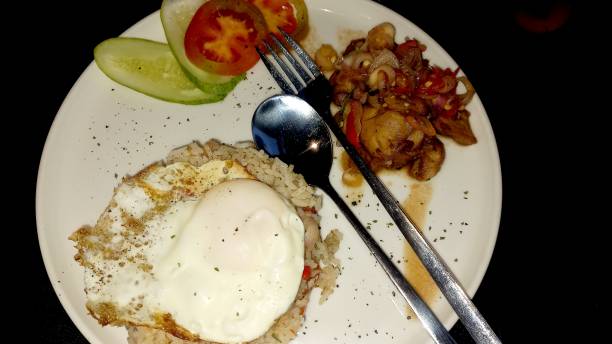 view of spicy fried rice and egg, served with raw shallot sauce, sliced cucumber and tomato, on a white porcelain plate, cutlery - sweet sauce tablespoon food sweet food imagens e fotografias de stock