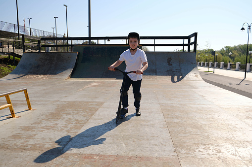 a cute boy in helmet is riding on bike in skate park.