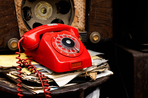 Viejo teléfono rojo y antiguo entre radios viejas y papeles photo