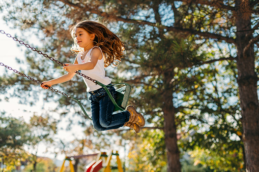 Cheerful little girl having fun swinging in the park