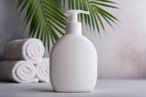 White blank packaging cosmetic plastic bottle with palm leaves. Bathroom and grooming product.