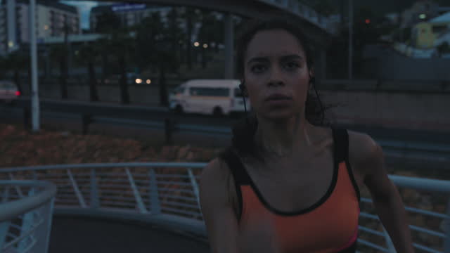 strong woman athlete running in urban city evening training jogging at night wearing fitness tracker slow motion