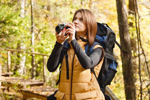 Young Caucasian Woman Hiker Taking Photos with Retro Film Camera in Autumn Forest