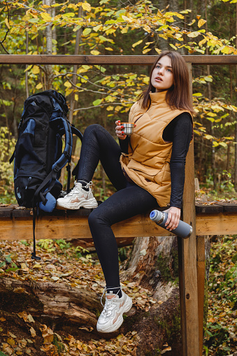 Woman traveler with thermos of coffee or tea in hand on a halt in a trip. Travel and camping concept. Warming drink, reflection in nature