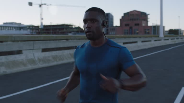 young african american athlete man running training intense cardio workout jogging on urban city road wearing earphones