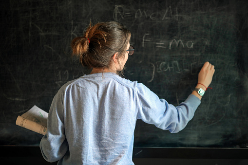 Senior female math teacher writing on board in classroom. She is in her fifties. This is part of a series promoting diversity and equity in STEM. Horizontal waist up indoors shot with copy space. This was taken in Montreal, Quebec, Canada.