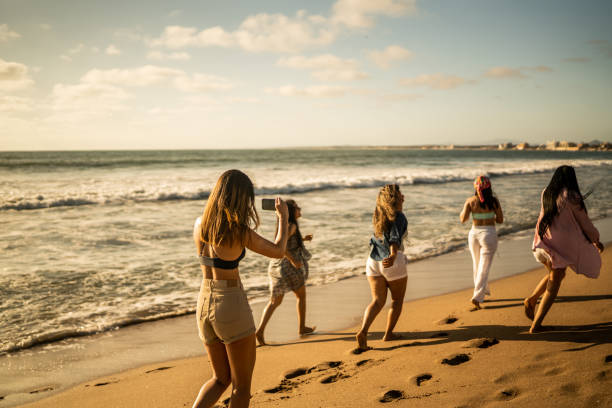 Female friends having fun and filming while walking on the beach