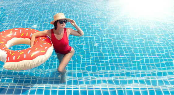 Beautiful young woman with inflatable donut ring relaxing in swimming pool. Summer vacation. With copy space