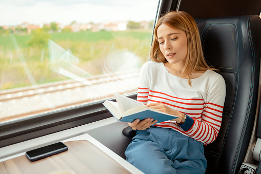 Young beautiful girl on a train reading a book while traveling in a train