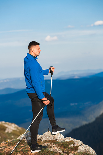 Young athlete man hiking and enjoying springtime on the mountain peak. Blue sportswear jacket and black Joggers.