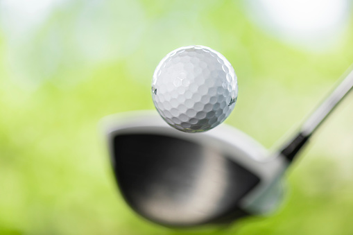 Golf ball swing action on golfer's first stroke with drivers. Close up of golf ball coming out after golf shot. Close up view of ball after crive hit on tee on golf course isolated  blur background