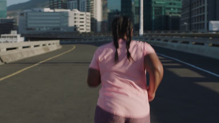 overweight woman runner exercising running weight loss challenge jogging in urban city at sunset rear view