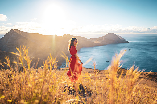 Description: Smiling woman in red dress enjoys the morning atmosphere on the foothills of a volcanic island in the Atlantic Ocean. São Lourenço, Madeira Island, Portugal, Europe.