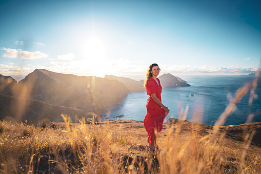 Description: Happy woman in red dress enjoys the morning atmosphere from the foothills of a volcanic island in the Atlantic Ocean. São Lourenço, Madeira Island, Portugal, Europe.
