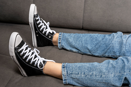 the girl's legs shod in classic sneakers. A sneakers on a girl's leg. Teenager's feet in casual new sneakers on the sofa close up image. Vintage style. concept image. Female feet in jeans and sports shoes