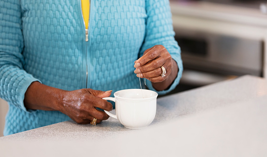 Cropped view of the hands of a senior African-American woman making herself a cup of tea in the kitchen.