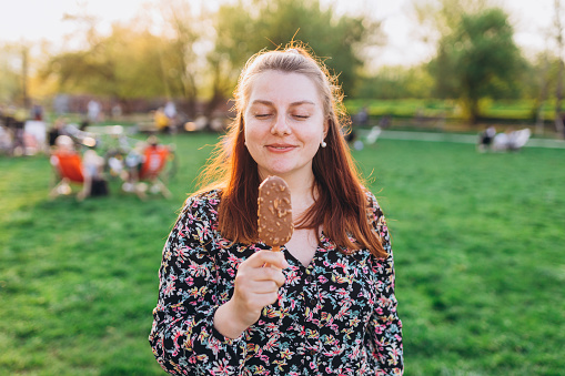 Happy young woman with delicious chocolate ice cream outdoors. Unhealhty food and weight loss concept. Summer time