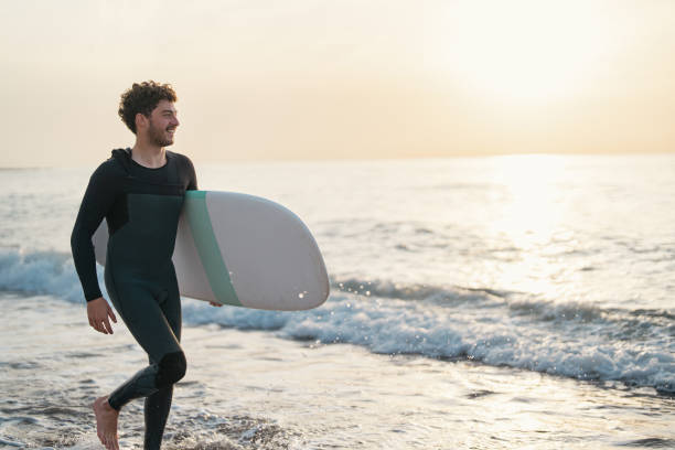 istock Surfer in wet suit, running on the beach during sunset 1489848994