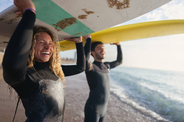 Young female and male surfers carrying their surfboards above the head stock photo