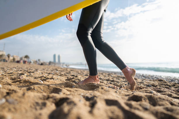 istock Unrecognizable man in wet suit, walking on the beach while carrying surfboard 1489850435