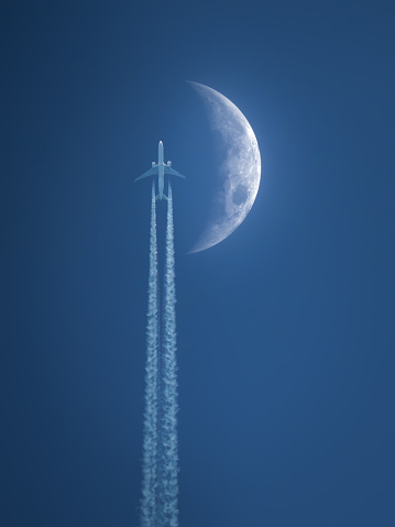 moon and airplane in a blue sky with vapor trail