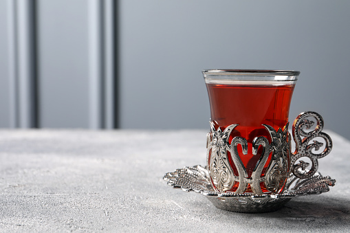 Glass of traditional Turkish tea in vintage holder on light grey table. Space for text