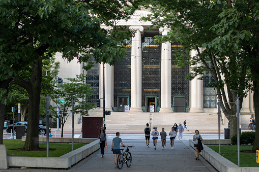 Cambridge, MA, USA - June 28, 2022: Students on the campus of the Massachusetts Institute of Technology in Cambridge, Massachusetts. Rogers Building (MIT Building 7) is seen in the background.