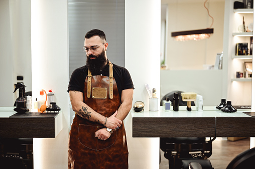 Fashionable hairdresser in a leather apron with  arms crossed.