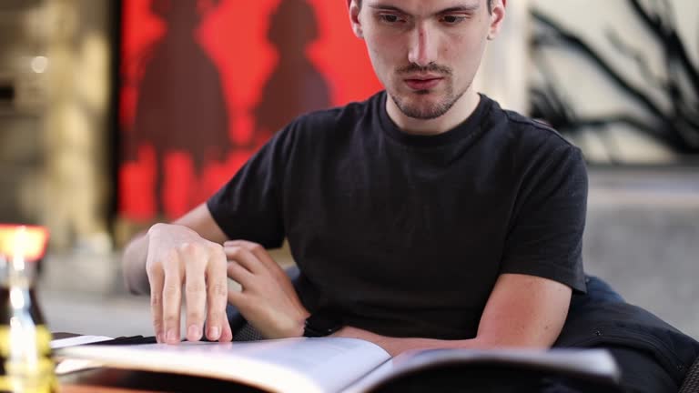 A man sits at a table on a street terrace and flips through a menu.