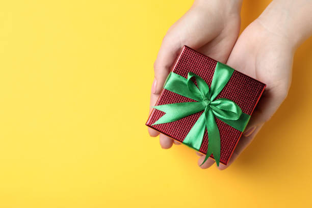 istock Woman holding beautifully wrapped Christmas gift box on yellow background, top view. Space for text 1489902027