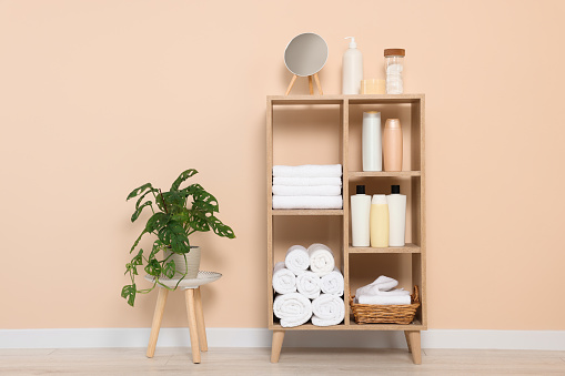 Soft folded towels and cosmetic bottles on wooden shelving unit near beige wall
