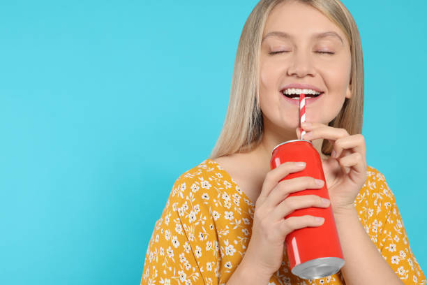 istock Beautiful happy woman drinking from red beverage can on light blue background. Space for text 1489905604