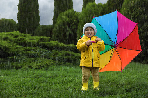 Cute little girl holding colorful umbrella and standing in garden, space for text