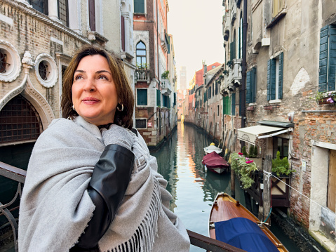 Winter in Venice, Italy concept: Travel and vacation destination background. Female tourist posing in a pashmina on a canal bridge in Venice on a cold sunny day