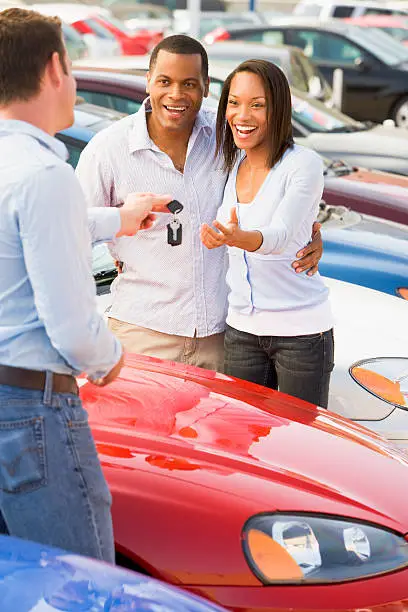 Couple collecting new car keys from salesman on lot smiling