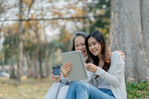 istock Grown daughter with aging mother expressing love and looking at tablet computer under tree in public park. 1489928485