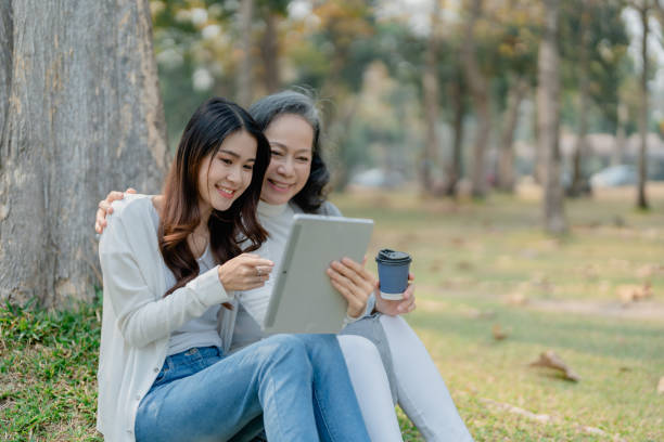 istock Grown daughter with aging mother expressing love and looking at tablet computer under tree in public park. 1489928524