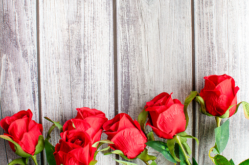 A top view of Valentine's Day concept. Red rose flower and beautiful green leaves on wooden table in under corner. Close-up, Selective focus, copy space on right for the design, text. Wood background
