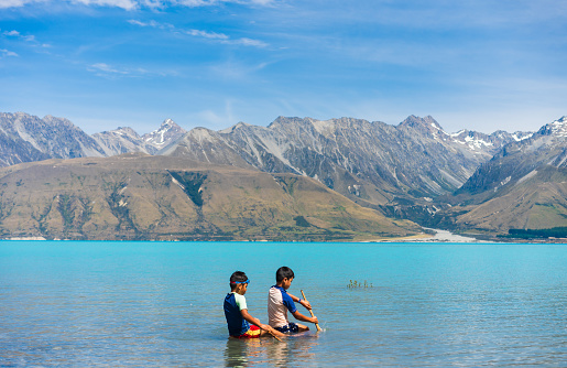 Joyful kids splash in Lake Pukaki's turquoise waters, surrounded by Southern Apls of South Island, New Zealand.