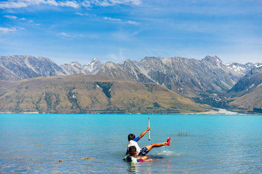 Joyful kids splash in Lake Pukaki's turquoise waters, surrounded by Southern Apls of South Island, New Zealand.