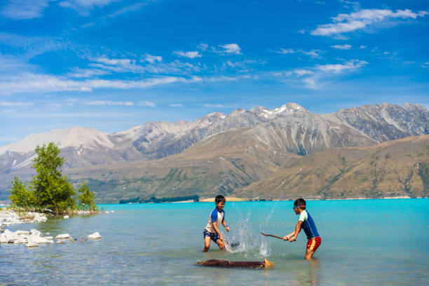 Joyful kids splash in Lake Pukaki's turquoise waters, surrounded by Southern Apls of South Island, New Zealand.